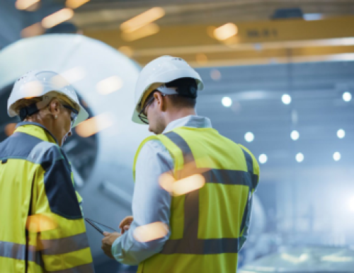 Photograph of two people wearing hard hats and high visibility jackets reviewing a piece of machinery